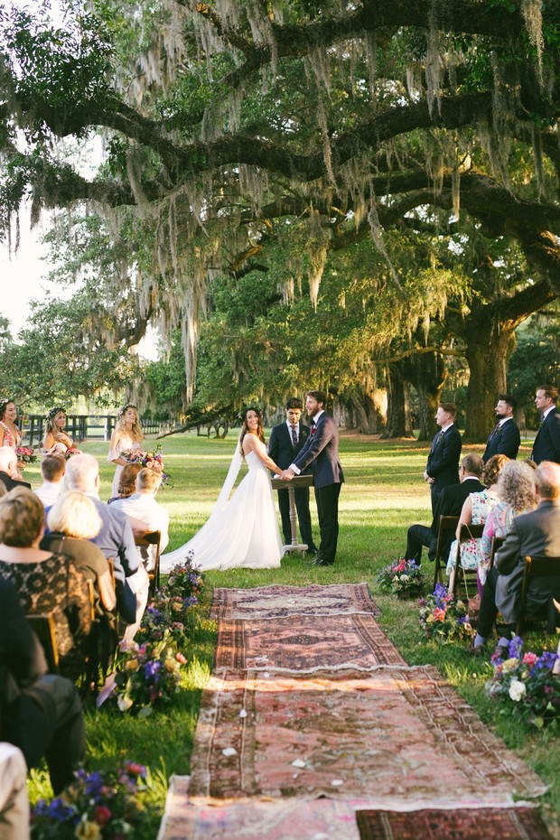 Outdoor wedding ceremony under mossy trees with floral aisle