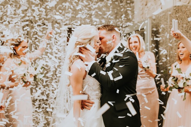 Joyful wedding kiss with confetti and bridal party