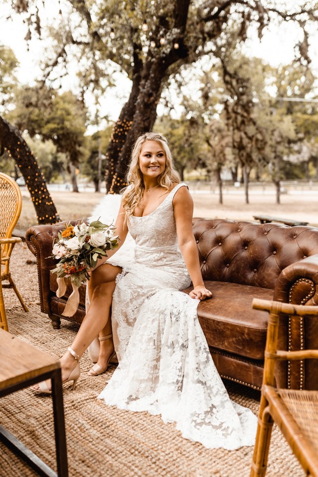 Bride in lace wedding dress sits on a leather couch outdoors