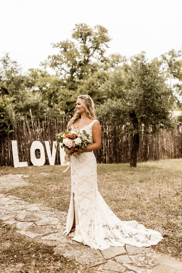 Bride in lace wedding gown holding flowers near LOVE sign