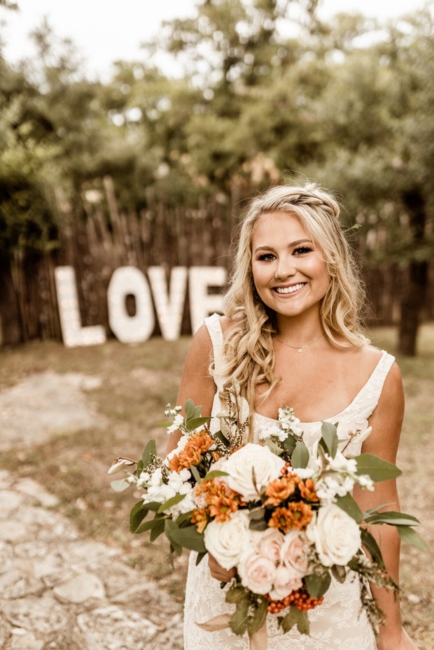 Bride with bouquet posing in front of LOVE sign outdoors