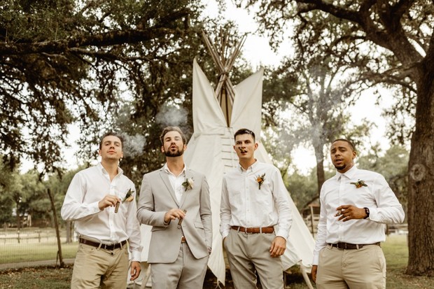 Groomsmen celebrate with cigars at outdoor wedding teepee