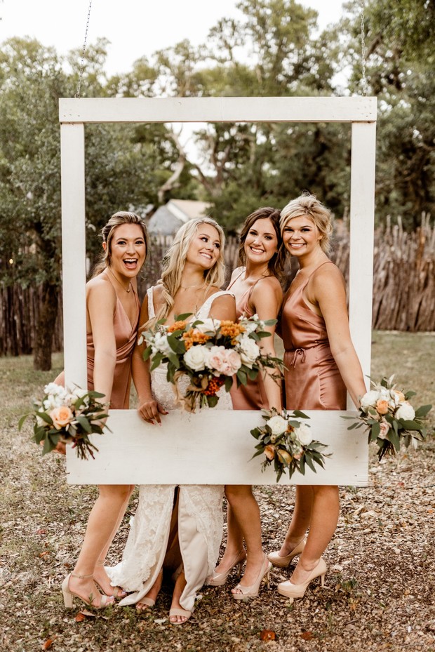 Bride and bridesmaids pose with a photo frame at wedding