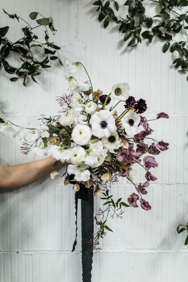Hand holds white and purple floral bouquet with black ribbon