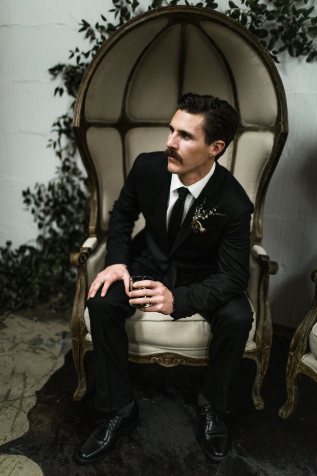 Man with mustache in black suit sitting in throne chair