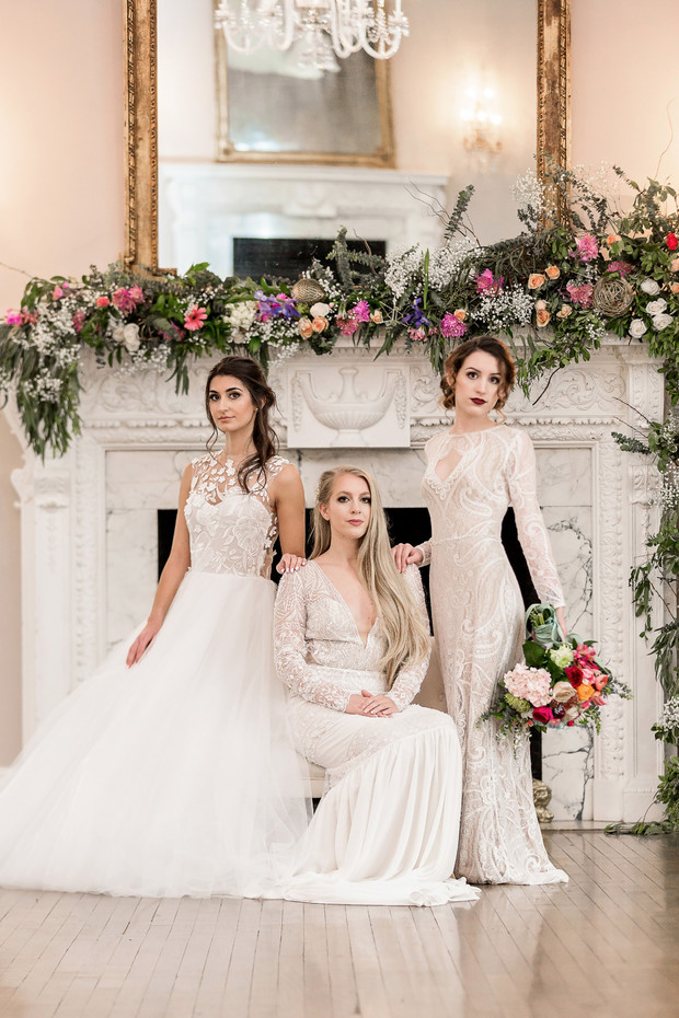 Bridesmaids in elegant white dresses pose by fireplace