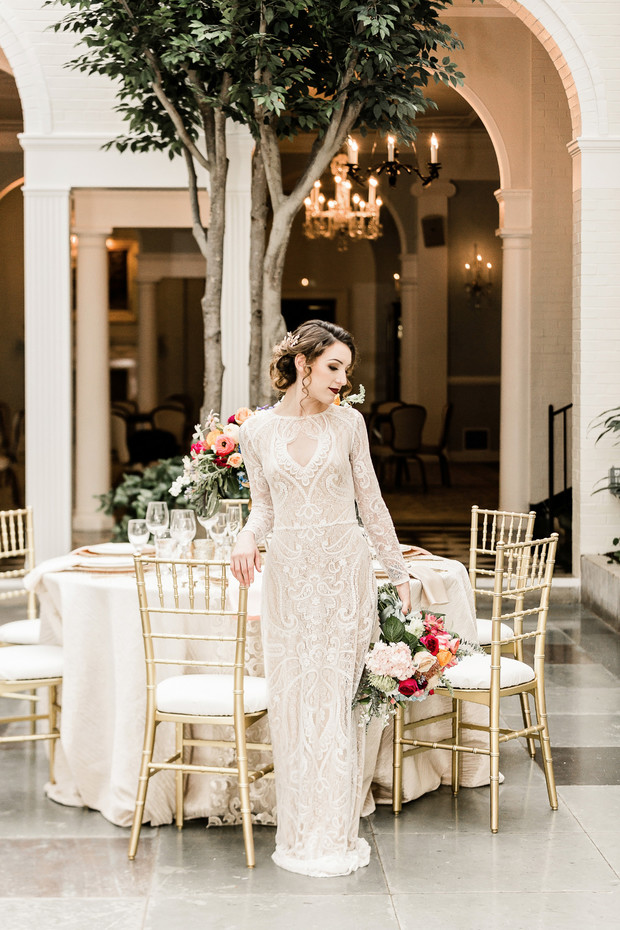 Bride in elegant lace gown poses near wedding reception table