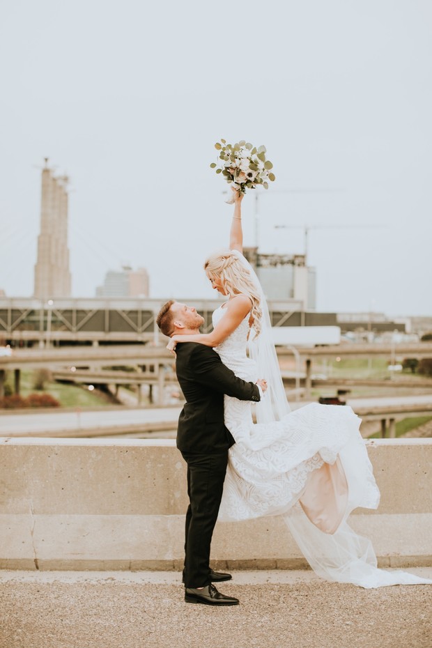 Joyful groom lifts bride holding bouquet urban wedding