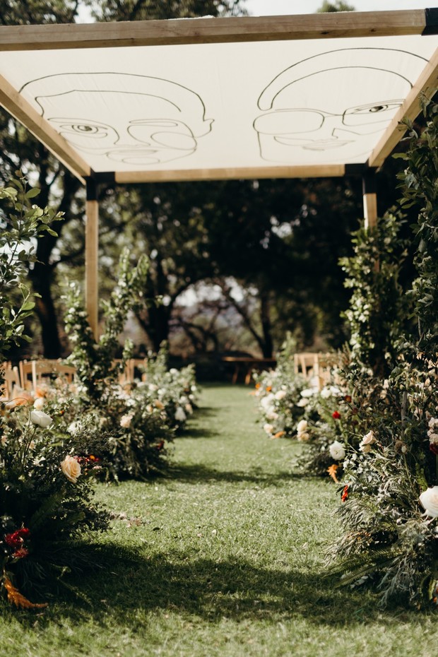 Wedding ceremony aisle with floral arrangements under a canopy featuring couple