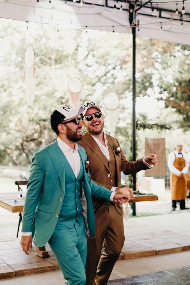 Grooms celebrate in suits and caps at outdoor wedding party