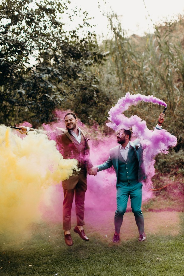 Gay couple jumping with colorful smoke grenades on wedding day