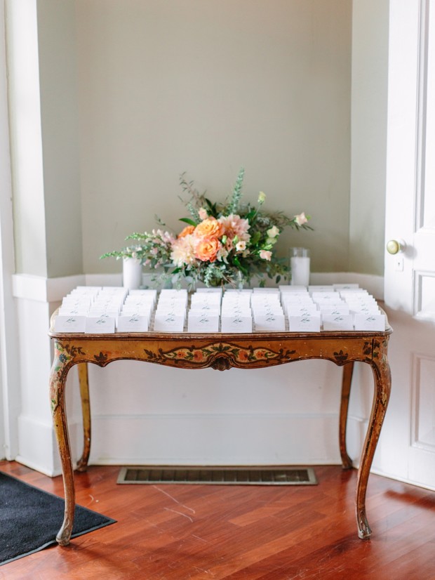 Wedding seating cards displayed on a decorative antique table with flowers