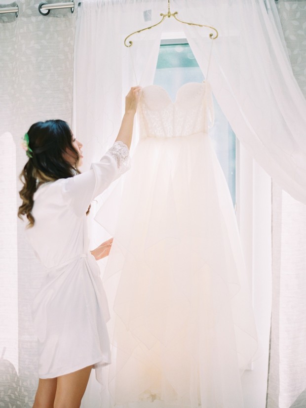 Bride admires her wedding dress hanging by the window