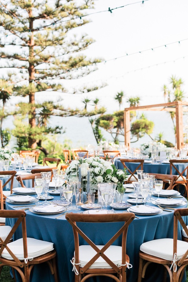 Outdoor wedding reception with blue linens and wooden cross-back chairs