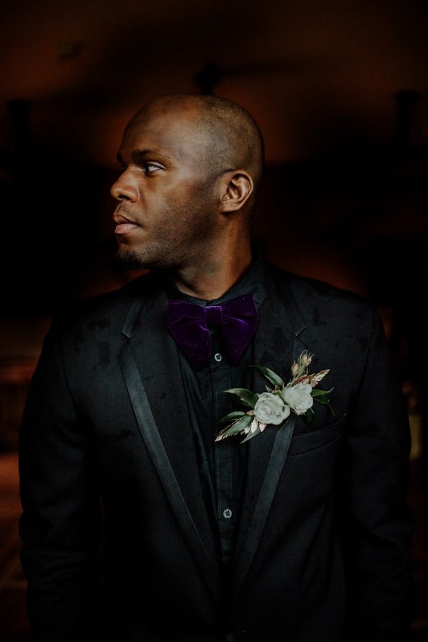 groom in all black and purple velvet bow tie