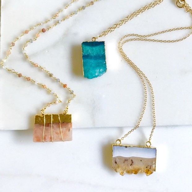 Three unique gemstone necklaces with golden chains on marble