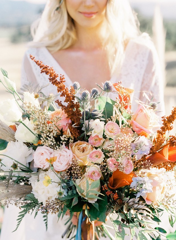 Bride holds colorful rustic wedding bouquet outdoors