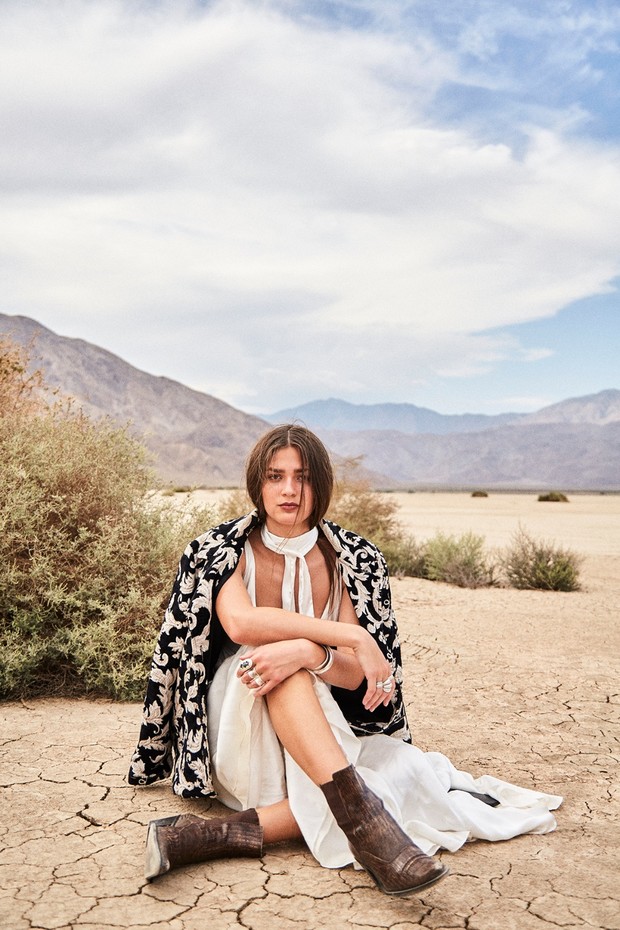Woman in dress and boots sitting in desert landscape