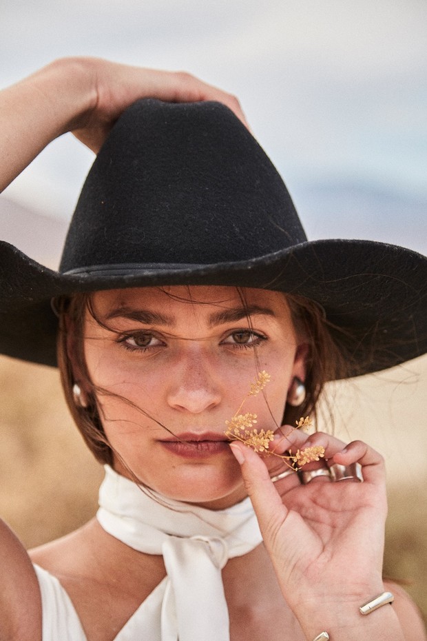 Portrait of a woman in a black hat holding a wildflower