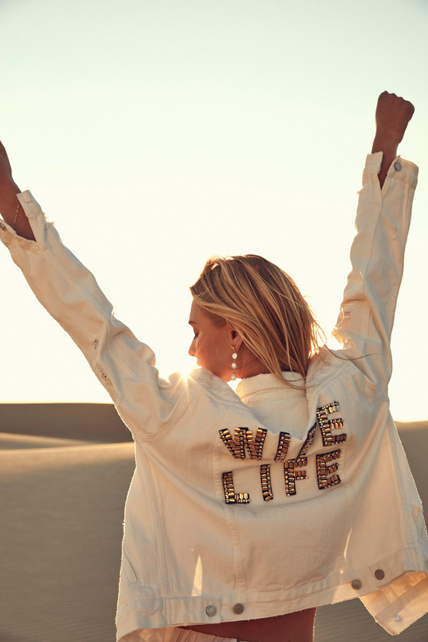 Woman with WIFE LIFE jacket celebrating on sunny dunes