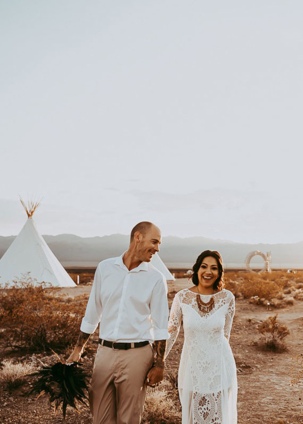 Happy couple in desert wedding attire near teepees
