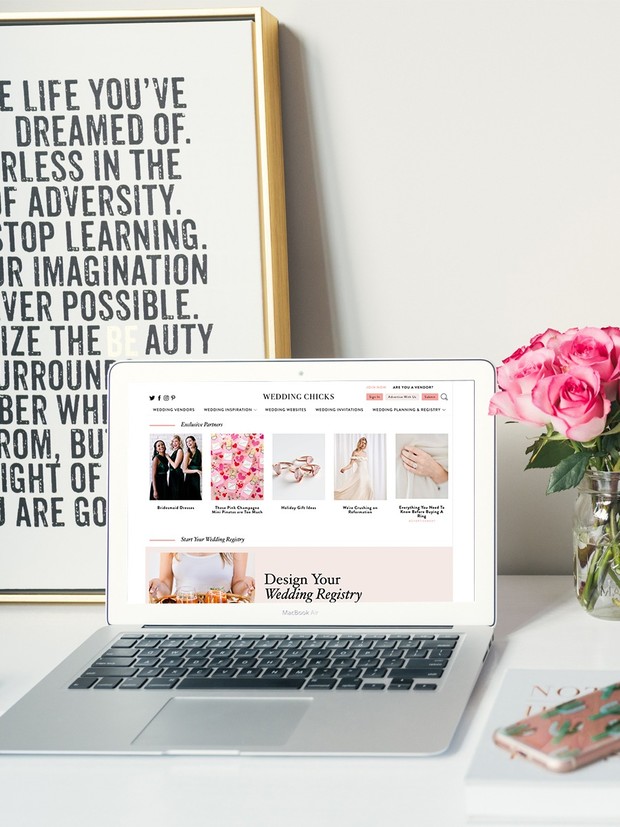 Laptop showing a wedding website next to a vase of pink roses