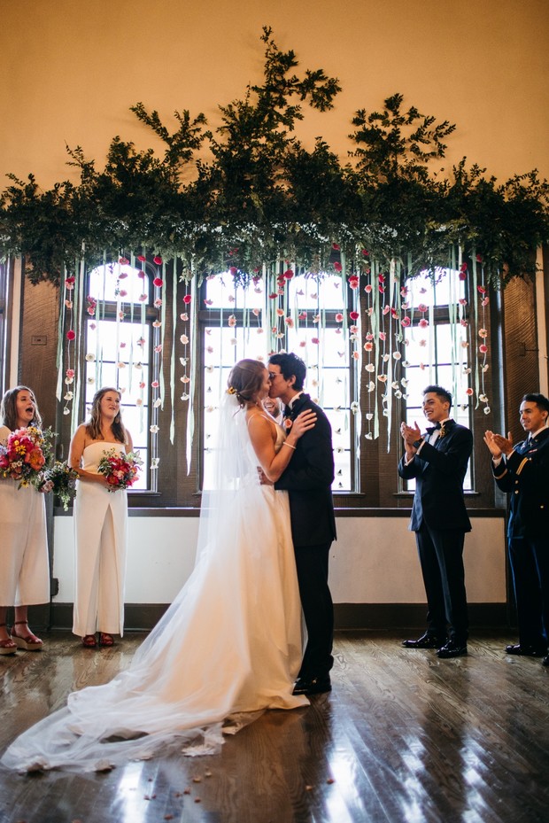 Bride and groom share a kiss at wedding ceremony under floral decor