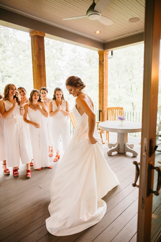 Bride showing off wedding dress with bridesmaids in the background