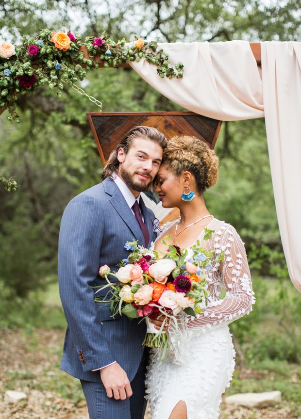 Happy couple embrace at a wedding ceremony with flowers and arch