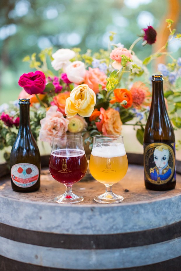 Beer glasses and bottles sit near flowers on a barrel table