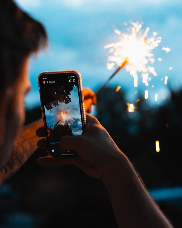 Person holding phone taking a photo of a sparkling firework