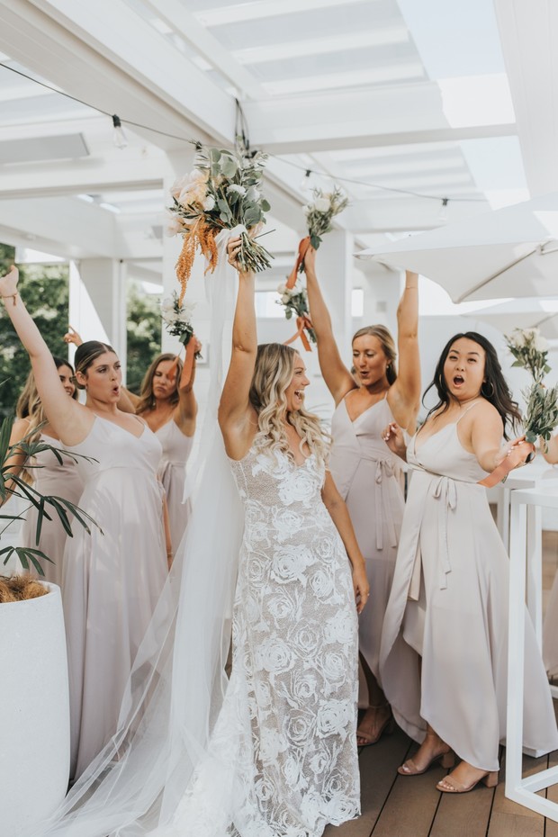 Bride and bridesmaids celebrating joyfully with bouquets in the air