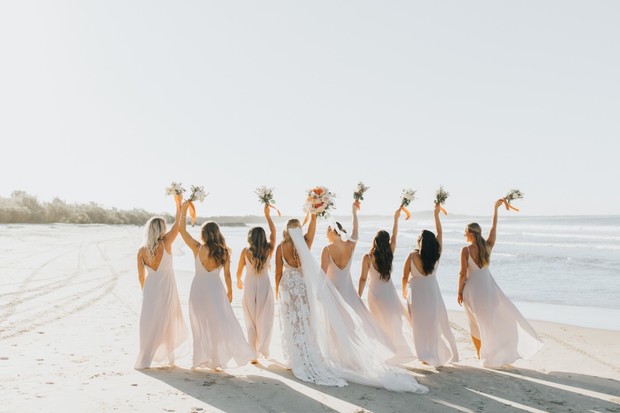 Bridesmaids and bride joyfully celebrating on the beach with flowers