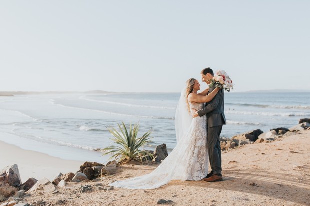 A bride and groom embrace on a sunny beach wedding day
