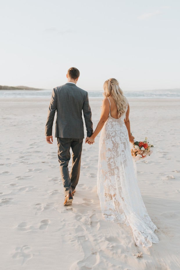 Newlyweds walking on a sandy beach at sunset, holding hands
