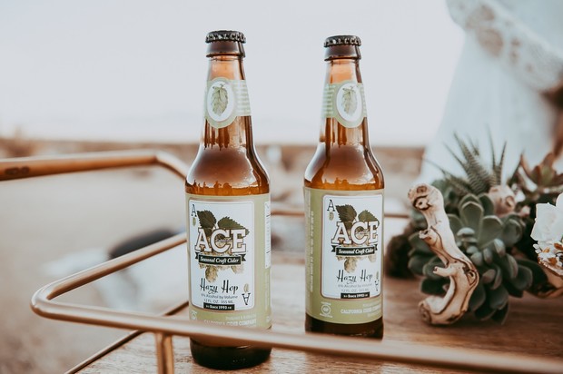Two ACE Seasonal Craft Cider Hazy Hop bottles on a rustic wooden tray