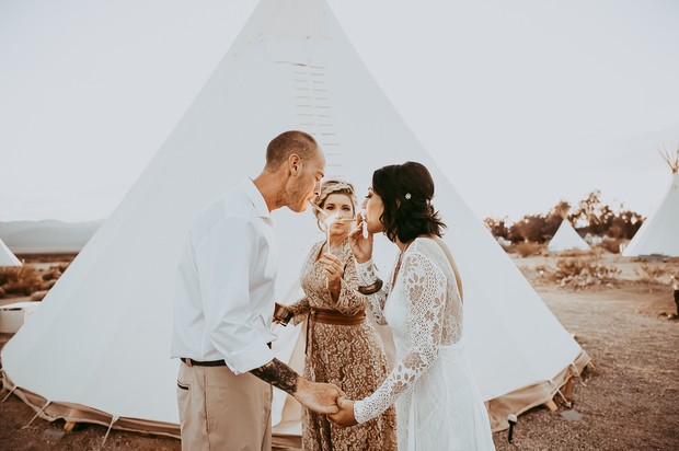 Couple lighting cigars at outdoor wedding with teepee backdrop