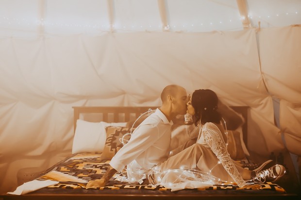 Romantic kiss shared between couple with fairy lights on a bed