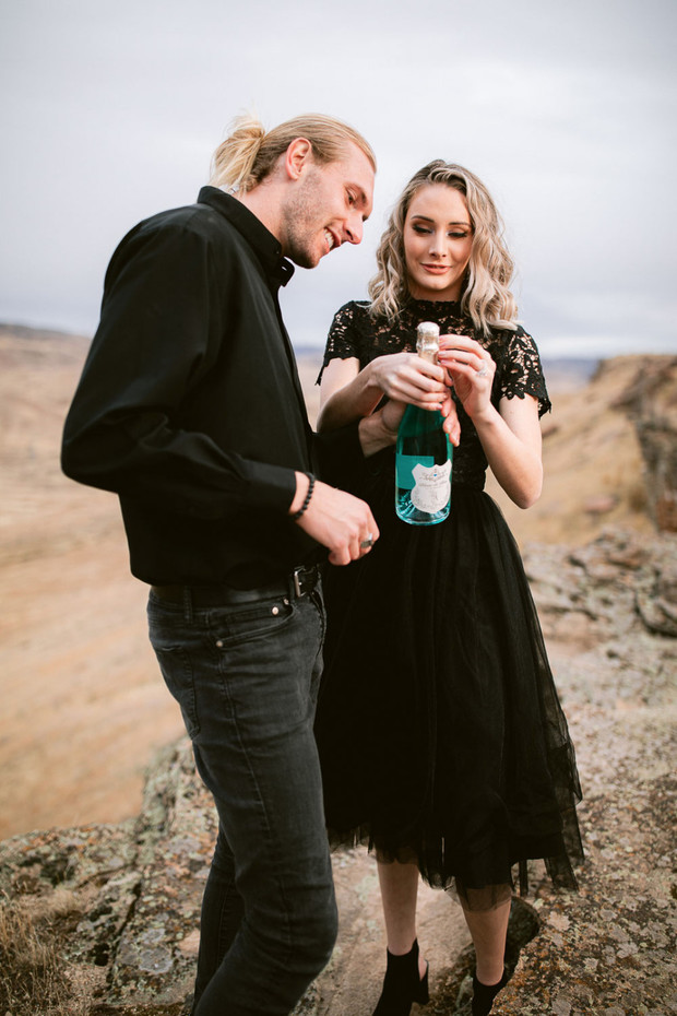 Romantic couple opening champagne bottle with mountain backdrop