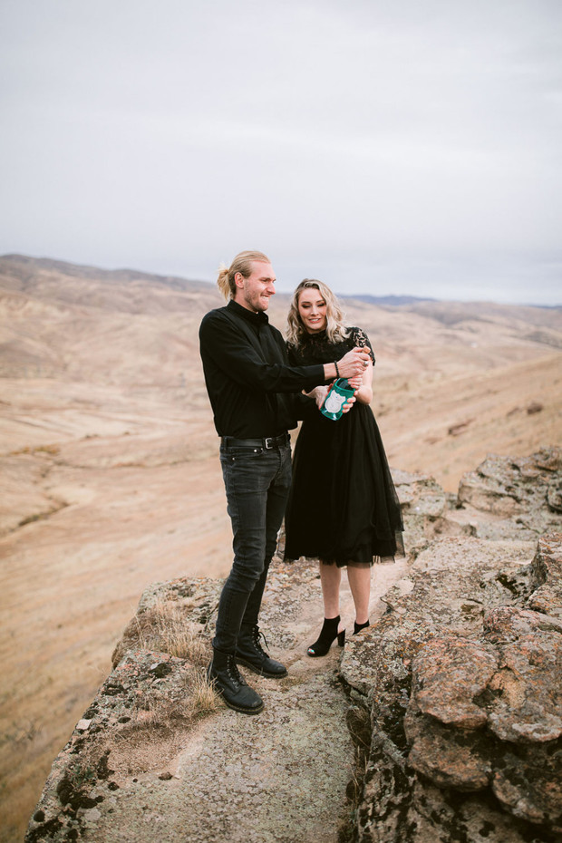 Couple popping champagne on a cliff during engagement photos