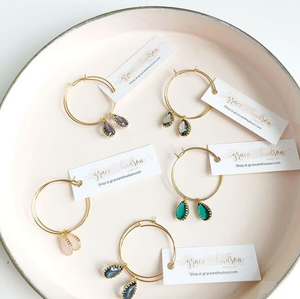 Gold hoop earrings with teardrop gems on a soft pink dish