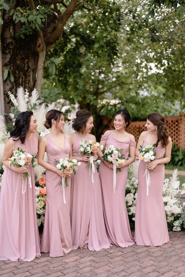 Bridesmaids in pink dresses smiling and holding bouquets outside