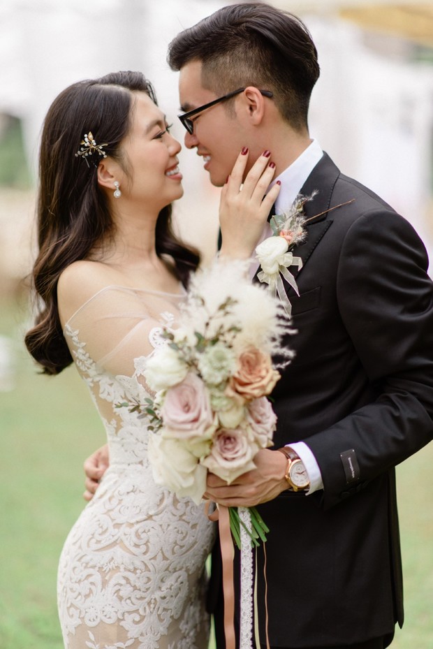 Happy couple embraces and smiles at their wedding day, holding a bouquet