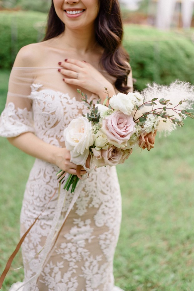Smiling bride holding a bouquet of roses, wearing a lace wedding dress