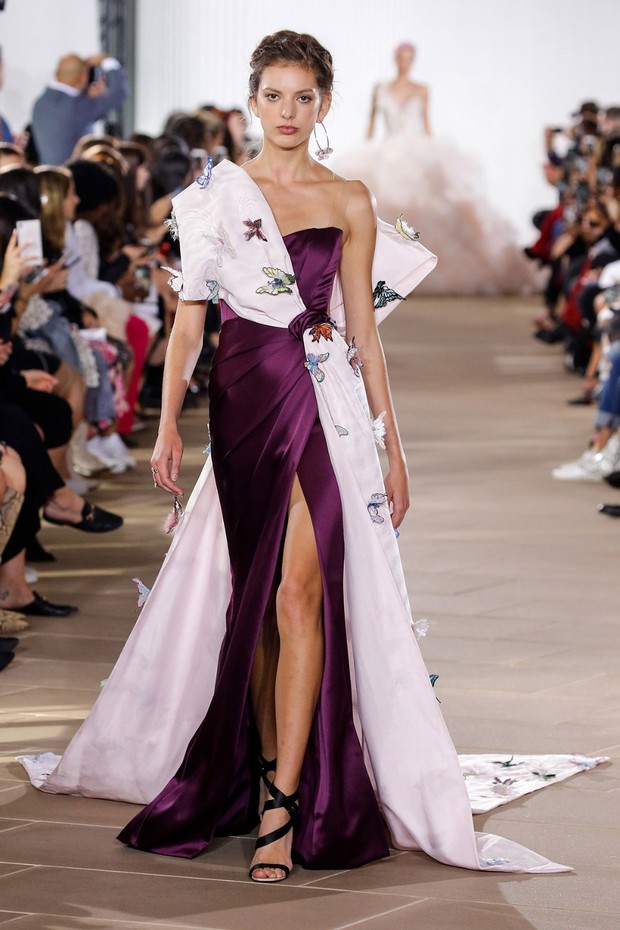 Fashion model in a butterfly-adorned, purple, one-shoulder gown on a runway