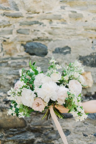 Elegant white and blush wedding bouquet in front of a stone wall