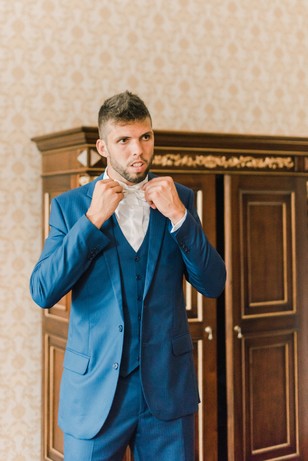 Groom adjusting bowtie in a blue suit before wedding