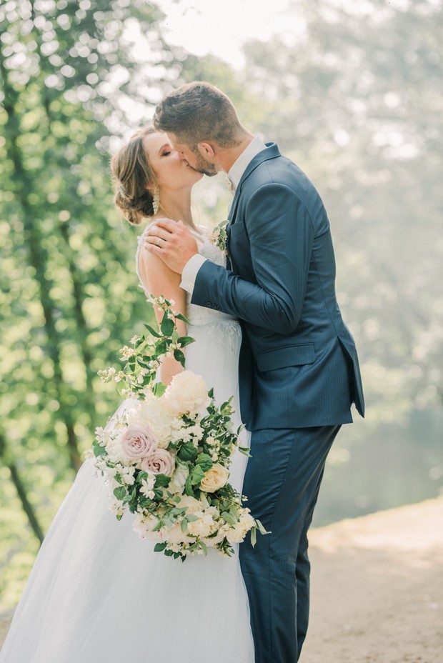 Romantic wedding kiss with bride and groom in a sunny forest