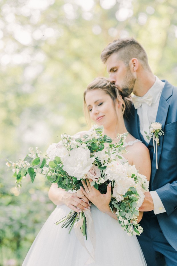 Bride holding bouquet kissed by groom on wedding day