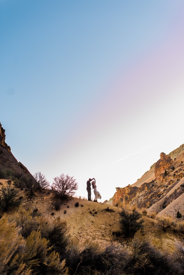 Couple dancing joyfully atop a desert hill at sunset